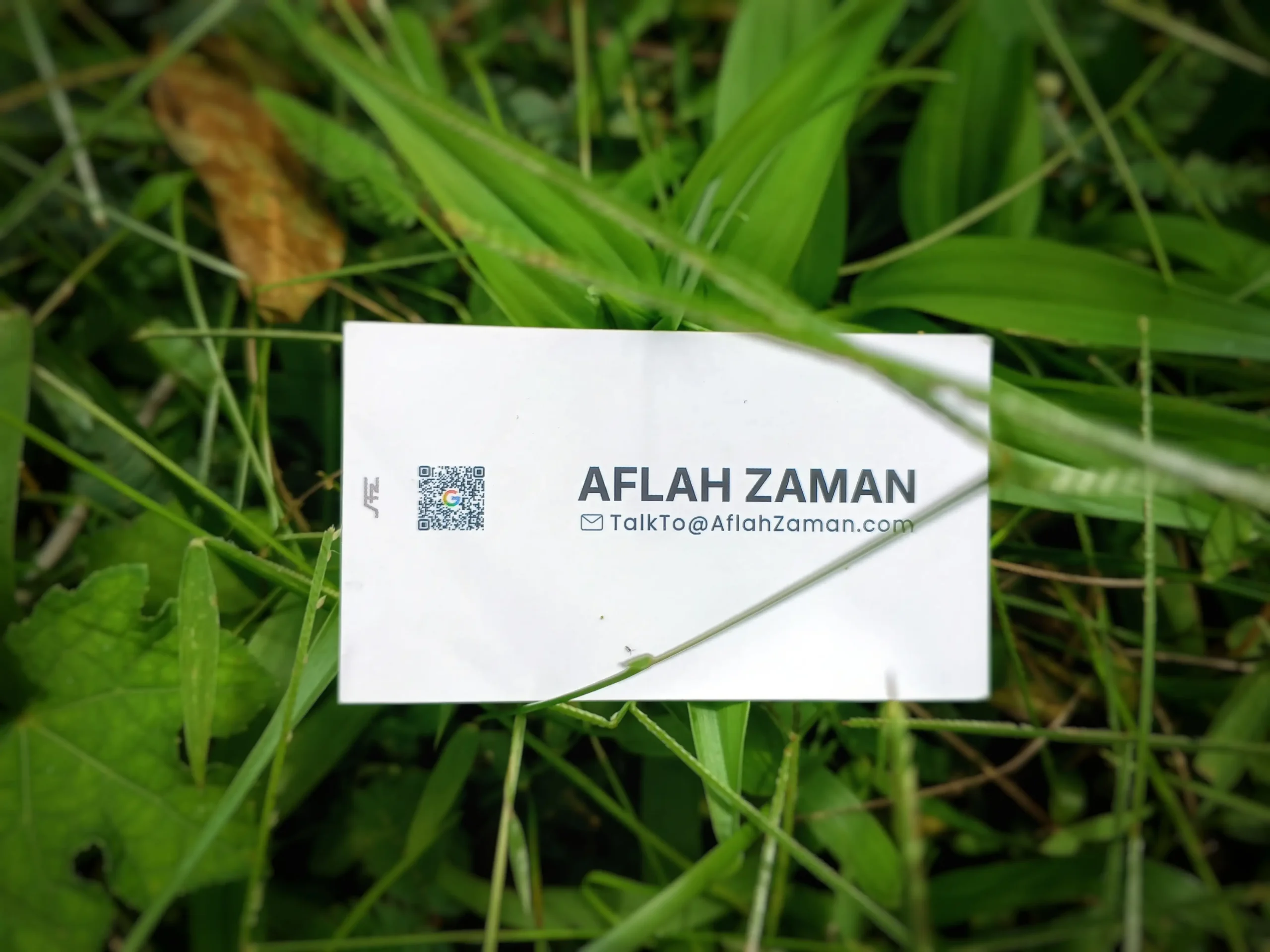 Aflah Zaman white minimalist business card with QR code, laid on green grass